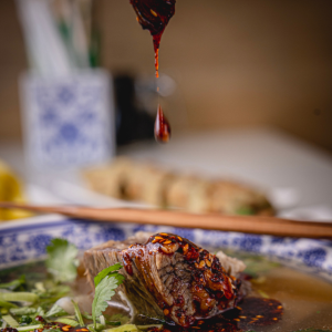 Dark chili oil dripping onto a slice of beef in a bowl of noodle soup.