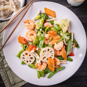 A white plate filled with colorful stir-fried shrimp, lotus root, and vegetables.