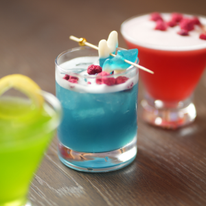 Three colorful cocktails, including a blue drink with gummy shark garnish.