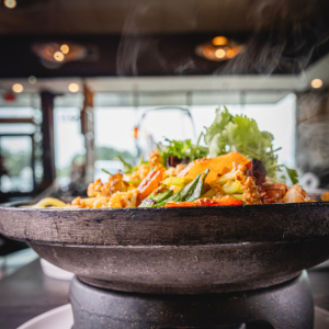 Steaming stir-fry dish with fresh vegetables served in a heated stone bowl.
