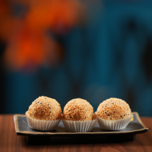 Three golden sesame seed balls served in paper liners on a rectangular plate.