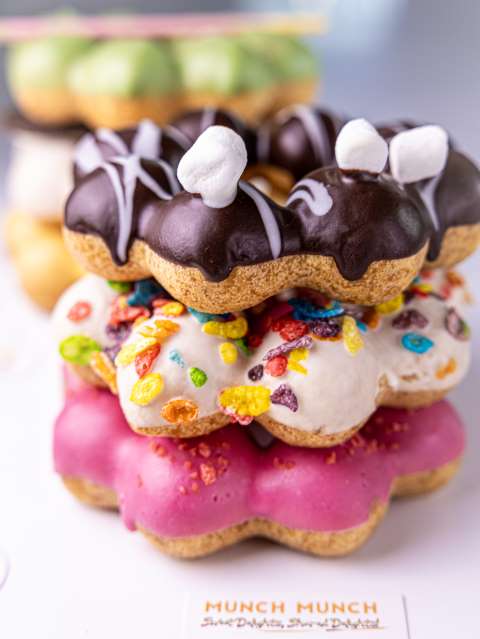 Stack of mochi donuts with chocolate, cereal, and pink glazes.